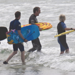 Thrre surfers entering water in Guernsey 